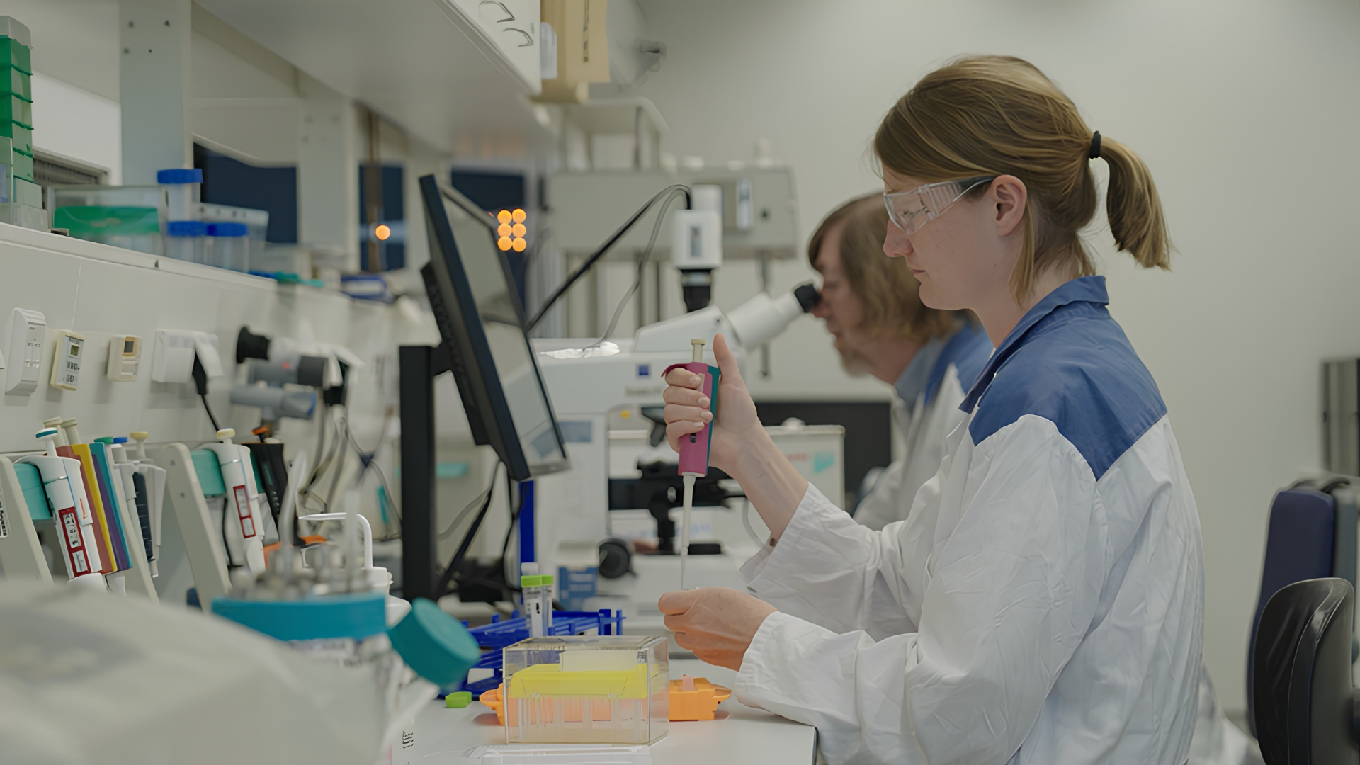 Uma mulher de jaleco e óculos de proteção utiliza uma pipeta em laboratório.