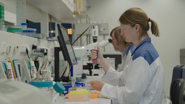 Uma mulher de jaleco e óculos de proteção utiliza uma pipeta em laboratório.