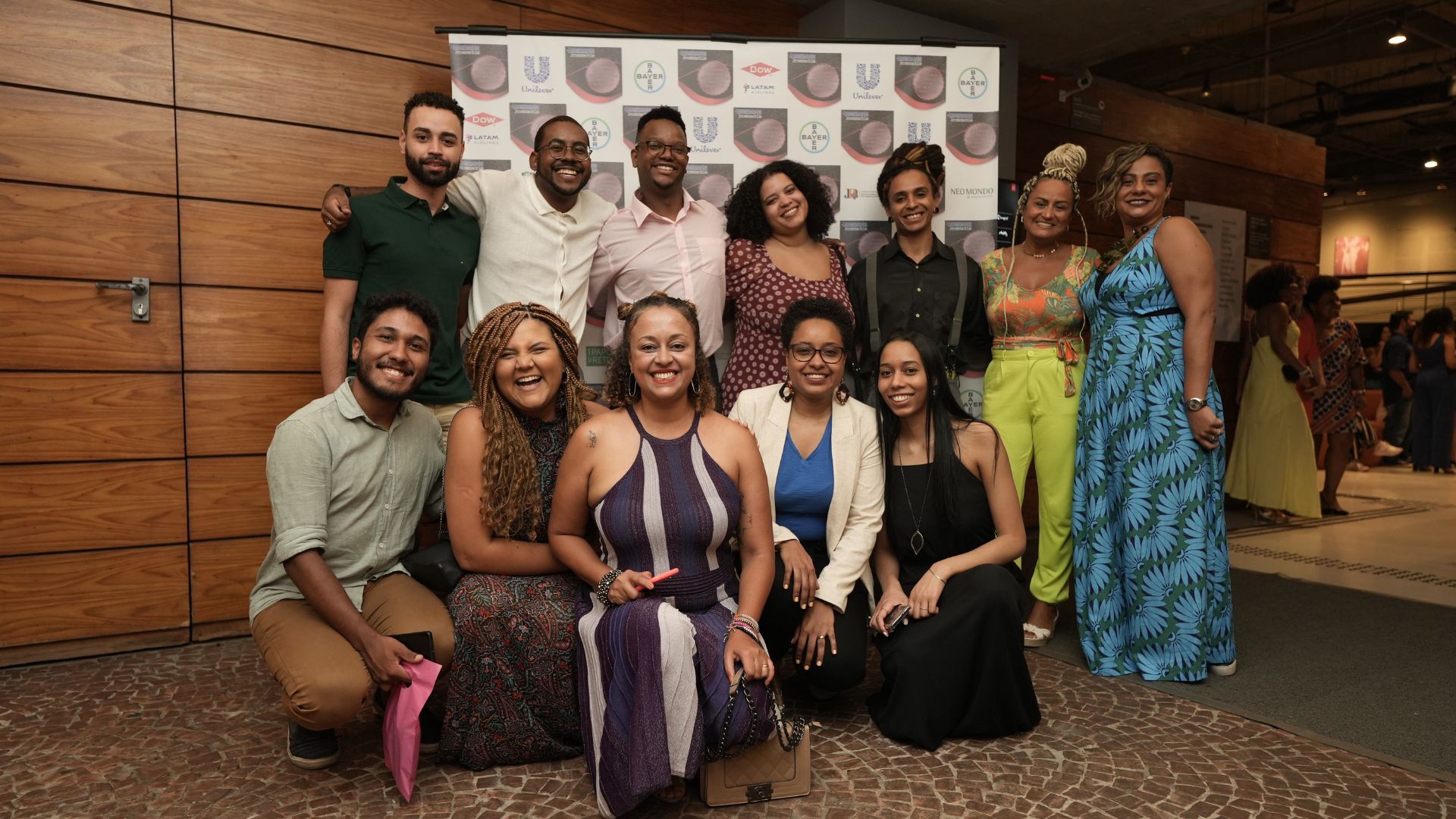 Time de Comunicação e Afrolever, atrás de painel branco com logo Unilever de outras empresas patrocinadoras do evento.