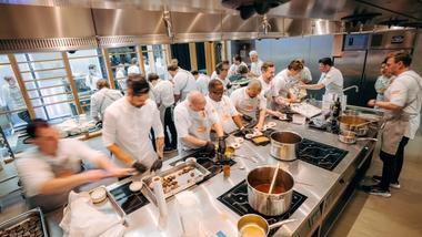 Uma equipe de chefs da Unilever Food Solutions prepara alimentos em uma cozinha movimentada, com várias panelas nos fogões.