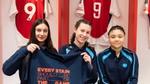 Três meninas sentadas no vestiário do Arsenal FC, segurando uma camiseta com a frase “Toda mancha deve fazer parte do jogo”.