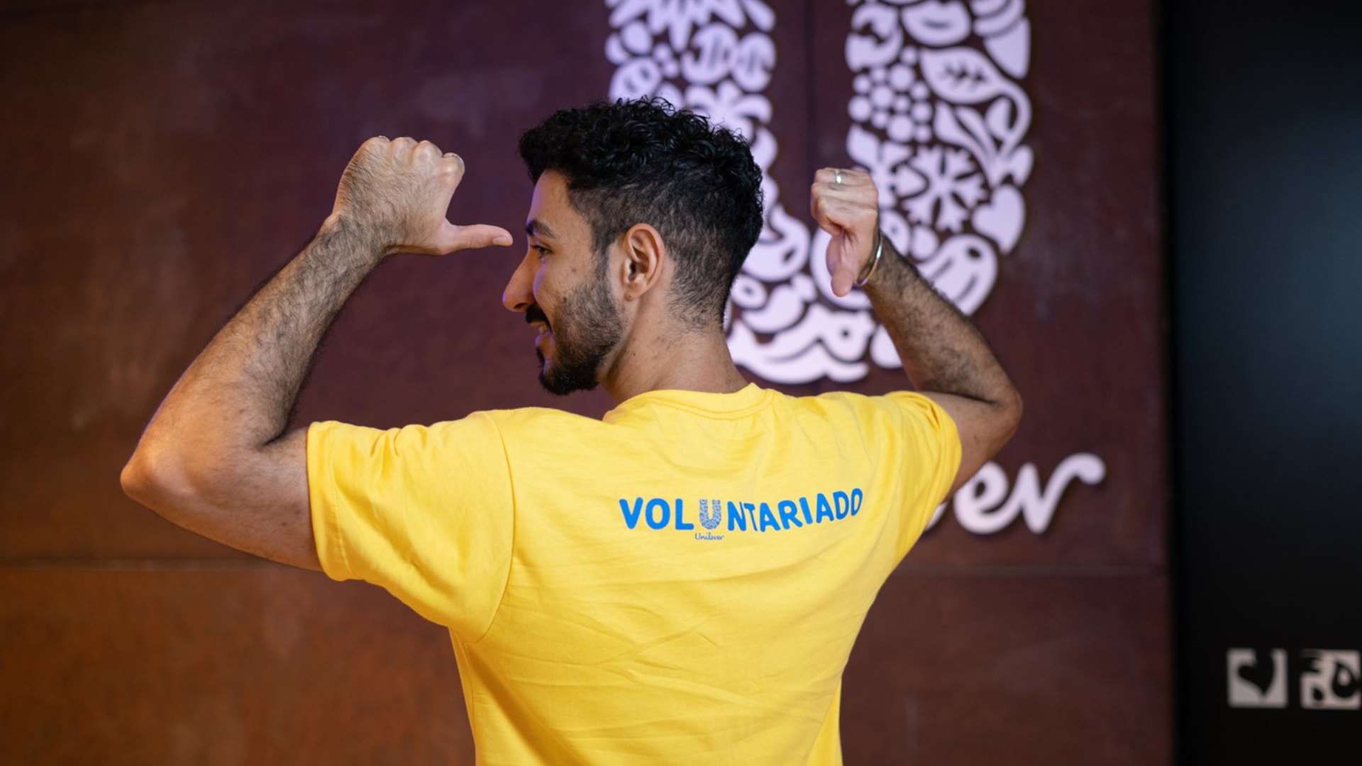 Homem de camiseta amarela escrita "voluntariado" nas costas.